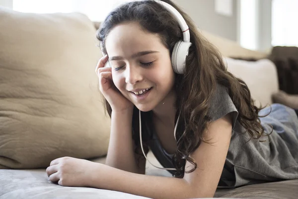 Vrouw luisteren muziek in hoofdtelefoons op sofa in kamer — Stockfoto