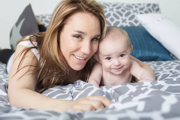 Retrato de madre joven y feliz con un bebé en la cama en casa — Foto de Stock