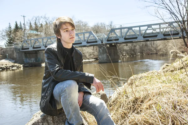 Adolescente se sienta fuera cerca de un puente chaqueta de cuero . — Foto de Stock