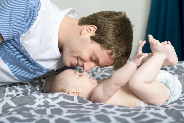 Retrato de jovem pai feliz com um bebê na cama em casa — Fotografia de Stock