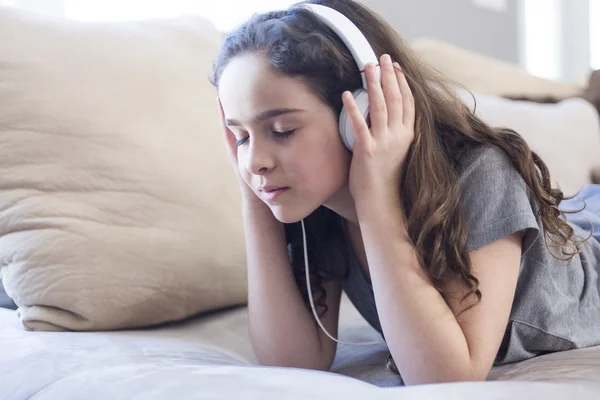 Vrouw luisteren muziek in hoofdtelefoons op sofa in kamer — Stockfoto