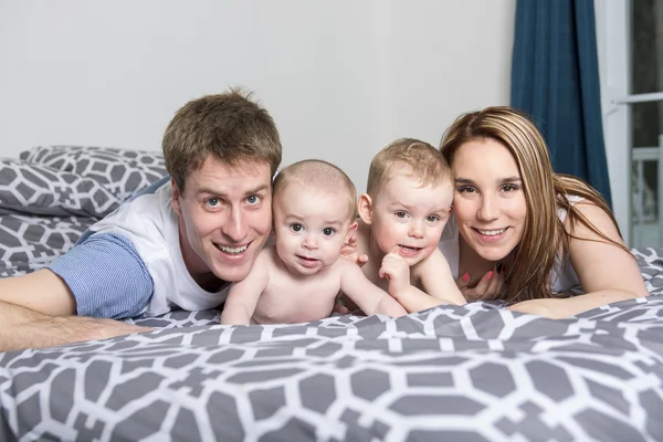 Famille heureuse de père, mère et bébé jouant au lit — Photo