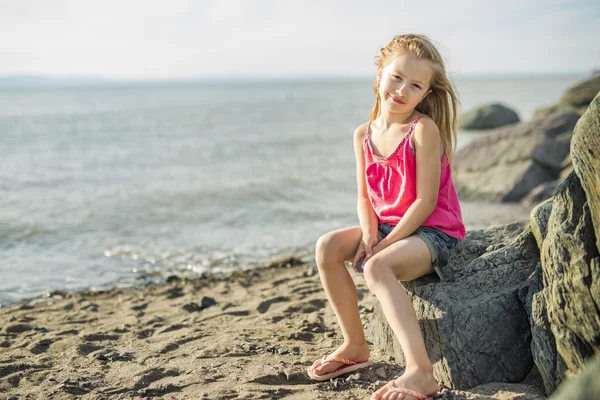 Söt liten flicka står nära stranden i solnedgången — Stockfoto