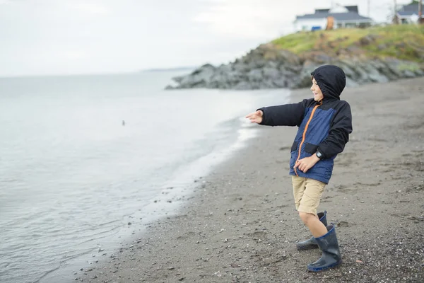 Pojken njuter av regnet och att ha kul utanför på stranden en grå regnig — Stockfoto
