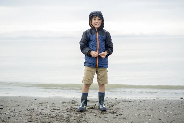 Pojken njuter av regnet och att ha kul utanför på stranden en grå regnig — Stockfoto