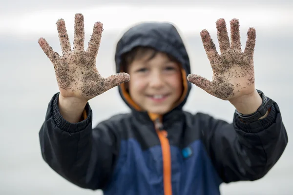 Pojken njuter av regnet och att ha kul utanför på stranden en grå regnig — Stockfoto