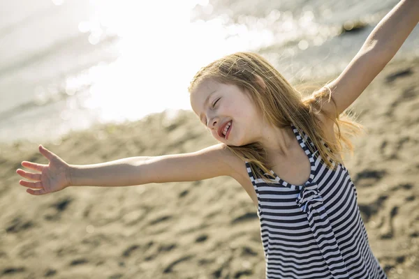 Roztomilá holčička stojící na pláži při západu slunce — Stock fotografie