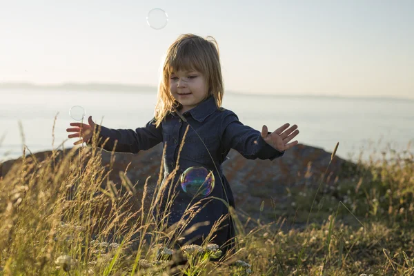 Nettes kleines Mädchen, das bei Sonnenuntergang in Strandnähe steht — Stockfoto