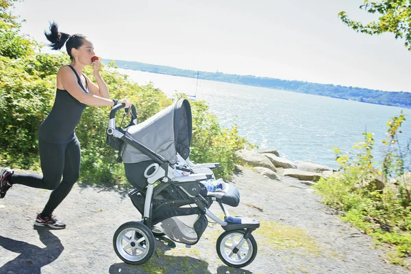 A Young mother jogging with a baby buggy — Stock Photo, Image