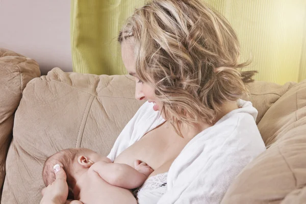 Uma mãe alimentando seu bebê no sofá — Fotografia de Stock