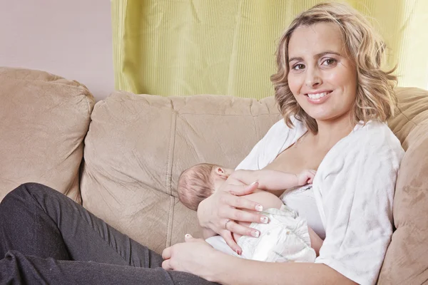 Uma mãe alimentando seu bebê no sofá — Fotografia de Stock