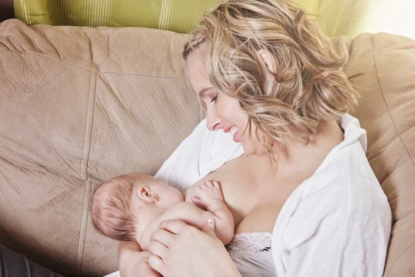 Uma mãe alimentando seu bebê no sofá — Fotografia de Stock