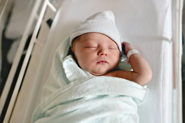 Новорожденный ребенок спит, пеленается в больничном одеяле и носит шляпу — стоковое фото