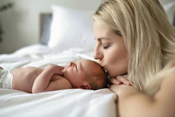 Женщина с новорожденным ребенком в постели целует ее — стоковое фото