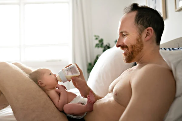 Um pai com um bebê recém-nascido na cama alimentando-se com leite — Fotografia de Stock