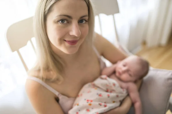 Giovane madre che tiene il suo bambino appena nato seduto su una sedia in soggiorno — Foto Stock