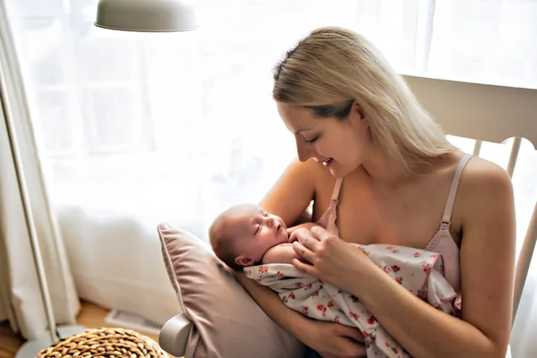 Giovane madre che tiene il suo bambino appena nato seduto su una sedia in soggiorno — Foto Stock