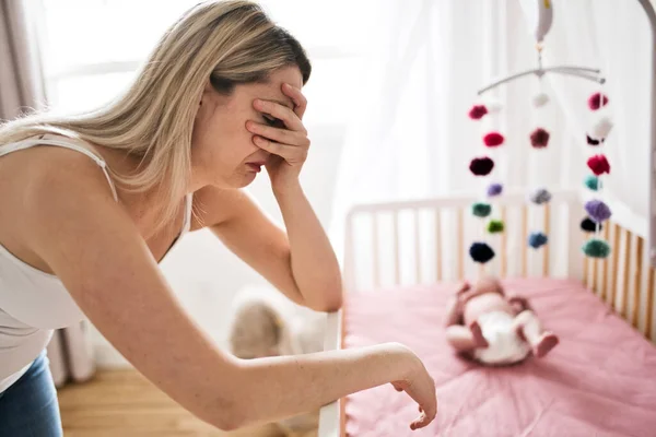 Mother suffering from postnatal depression near crib with cute baby at home — Stock Photo, Image