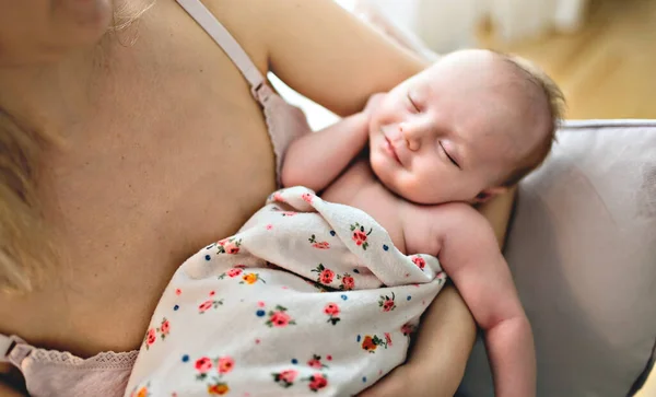 La giovane madre che tiene in braccio il suo bambino appena nato siede su una sedia in soggiorno. Vista da vicino sul bambino — Foto Stock