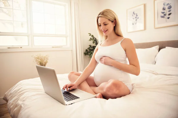 Attraktiv ung gravid kvinna med bärbar dator på sängen — Stockfoto