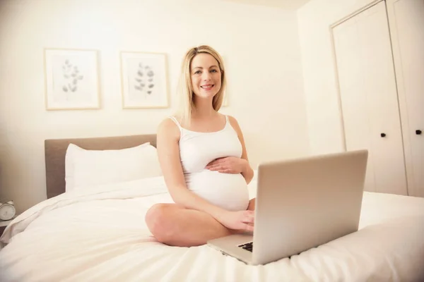 Attraente giovane donna incinta con computer portatile sul letto — Foto Stock