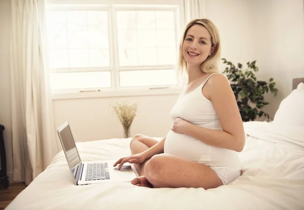 Attraente giovane donna incinta con computer portatile sul letto — Foto Stock