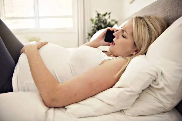 Mulher grávida na cama em casa com contrações segurando celular — Fotografia de Stock
