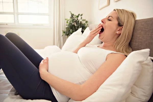 Беременная женщина на кровати дома зевает — стоковое фото