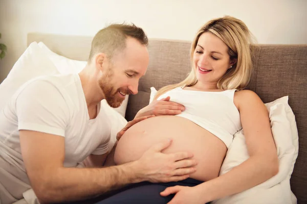 아름다운 임신 한 여성과 잘생긴 남편이 침대에서 함께 시간을 보내는 모습 — 스톡 사진