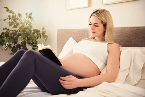 Zwanger vrouw op het bed thuis met boek — Stockfoto