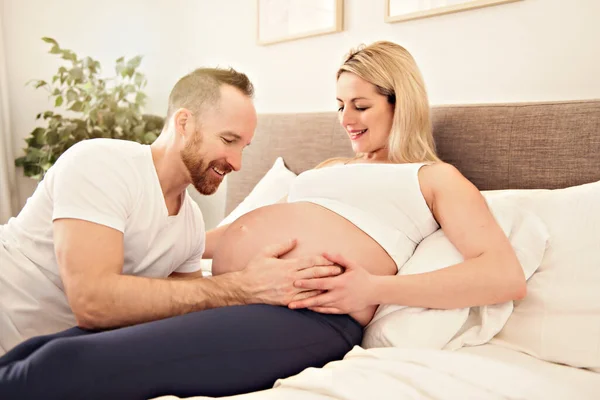 Красивая беременная женщина и ее красивый муж проводят время вместе в постели — стоковое фото