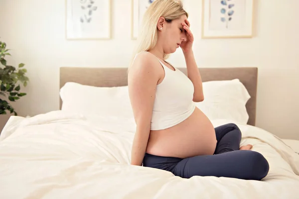 Mujer embarazada en la cama en casa con dolor de cabeza —  Fotos de Stock