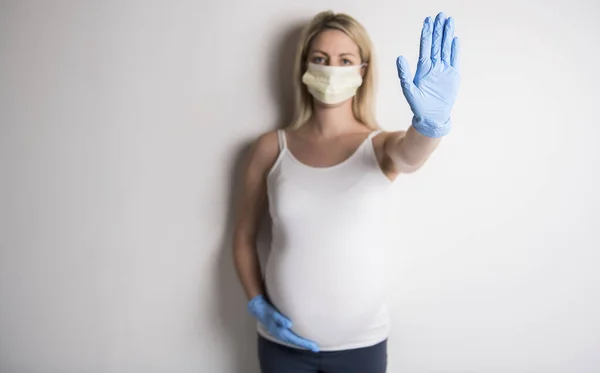 Zwangere vrouw in beschermende masker tegen infectieziekten en griep tonen stop gebaar met handschoen. Gezondheidszorgconcept. — Stockfoto