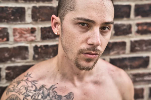 Muscular shirtless Caucasian man standing against brick wall with graffiti in urban setting — Stock Photo, Image