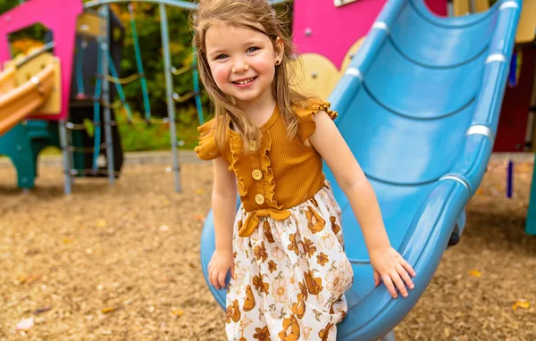 Happy Souriant enfant fille jouer à aire de jeux en plein air dans un beau parc sur une glissière — Photo