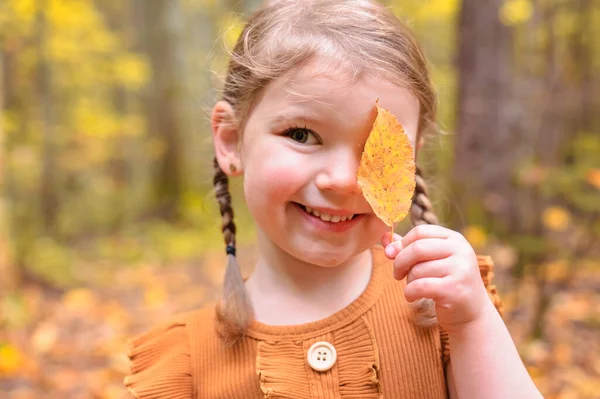 Mignon et de la mode enfant fille dans le parc d'automne tenant feuille — Photo