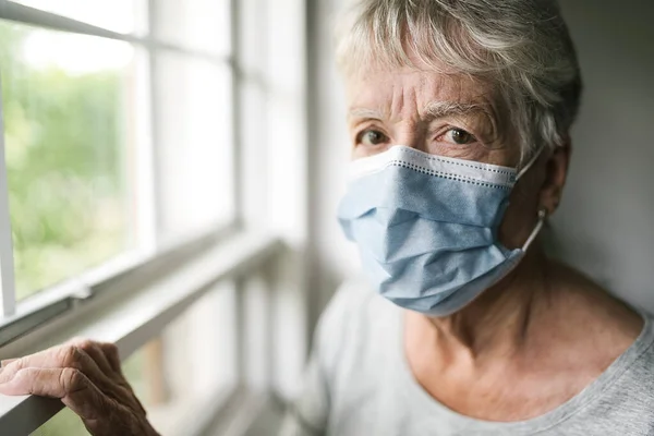 Een oudere vrouw met een beschermend masker voor het raam — Stockfoto