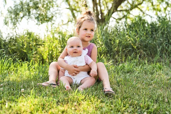 Heureuse adorable petite fille joufflue assise sur l'herbe avec sa fille sœur — Photo