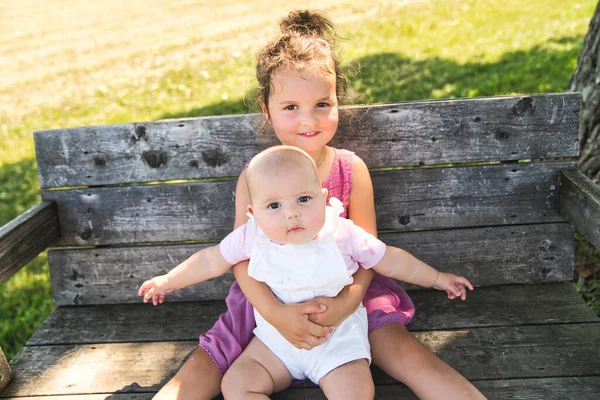 Happy adorable chubby baby girl sitting on a bench with her daughter sister — Stock Photo, Image