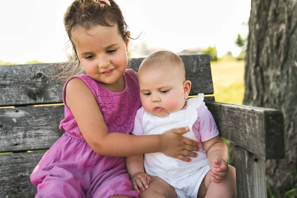Heureuse adorable petite fille joufflue assise sur un banc avec sa fille sœur — Photo
