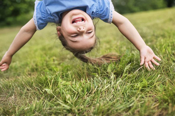 Divertente felice bambina in piedi sulla testa sull'erba nel parco. — Foto Stock