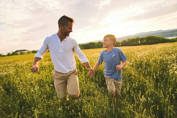 Felice famiglia di padre e figlio sul campo al tramonto divertendosi a camminare sull'erba — Foto Stock