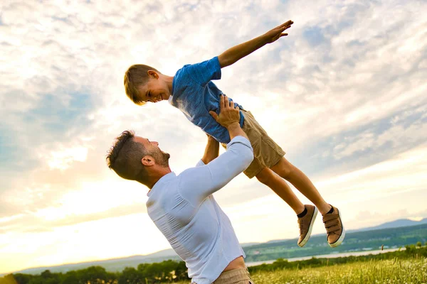 Szczęśliwa rodzina ojca i dziecka na polu o zachodzie słońca bawiąc się latając w powietrzu — Zdjęcie stockowe