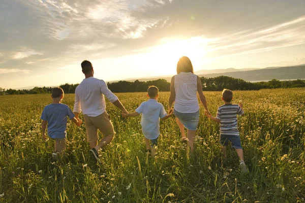 Szczęśliwa rodzina na polu stokrotki o zachodzie słońca mając wielki czas razem chodzenie pole — Zdjęcie stockowe