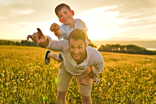 Gelukkig gezin van vader en kind op het veld bij zonsondergang plezier hebben op de vader terug — Stockfoto