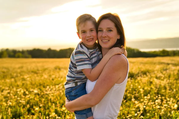 Família feliz de mãe e criança em campo ao pôr do sol se divertindo — Fotografia de Stock