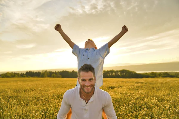 Famiglia felice di padre e figlio sul campo al tramonto divertirsi sul retro con la mano alta — Foto Stock