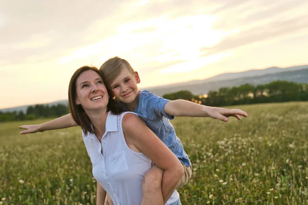 Famille heureuse de la mère et de l'enfant sur le terrain au coucher du soleil s'amuser — Photo