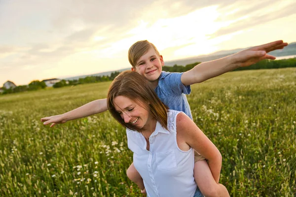 Felice famiglia di madre e bambino sul campo al tramonto divertendosi — Foto Stock