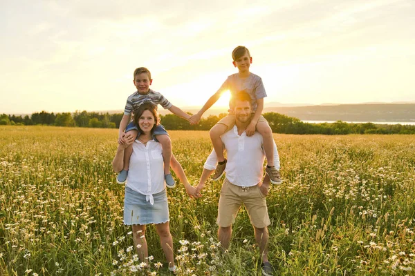 Famiglia felice sul campo margherita al tramonto divertendosi insieme — Foto Stock